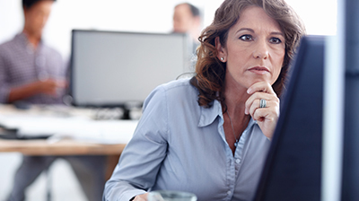 A woman working on her computer, coworkers in the background