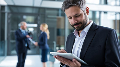 A businessman using a tablet, two coworkers are talking in the background